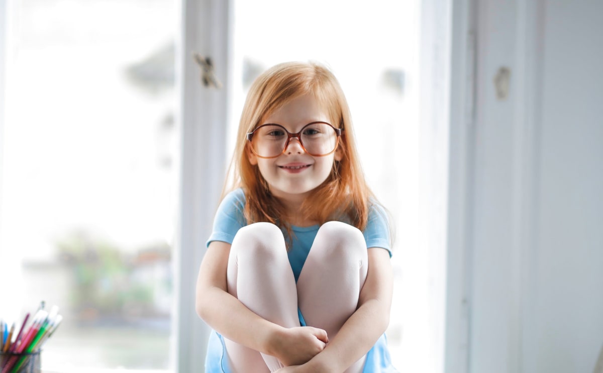 A little girl with glasses is smiling for the camera.