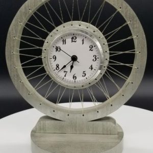 A clock is made out of metal and has a wheel on top.
